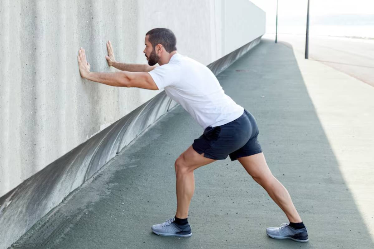 A person in athletic wear performs a wall stretch against a concrete surface, set against a serene outdoor backdrop.