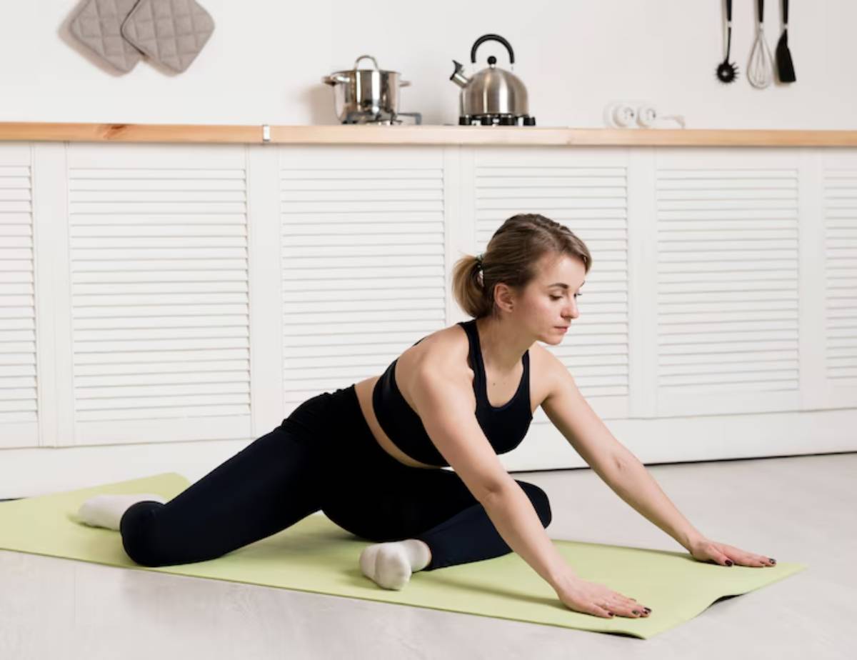 A person stretches on a green yoga mat in a bright kitchen, surrounded by cooking utensils and appliances.