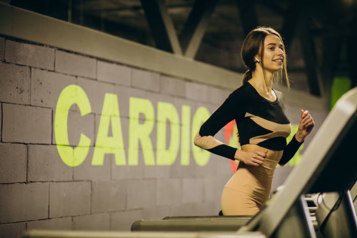 A woman exercises on a treadmill in a gym, with a bright green CARDIO sign on the wall behind her.