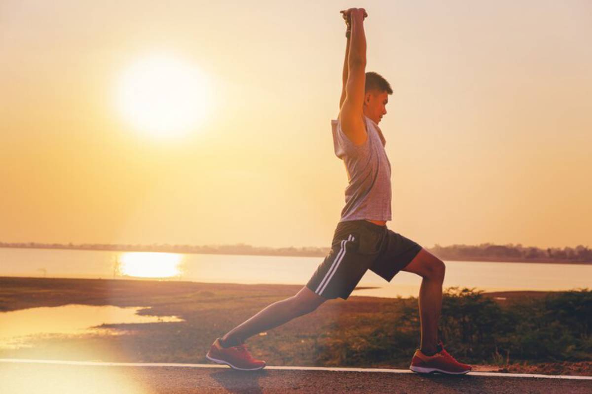 A person performs a lunge exercise on a road by the water during sunset, with vibrant hues illuminating the scene.
