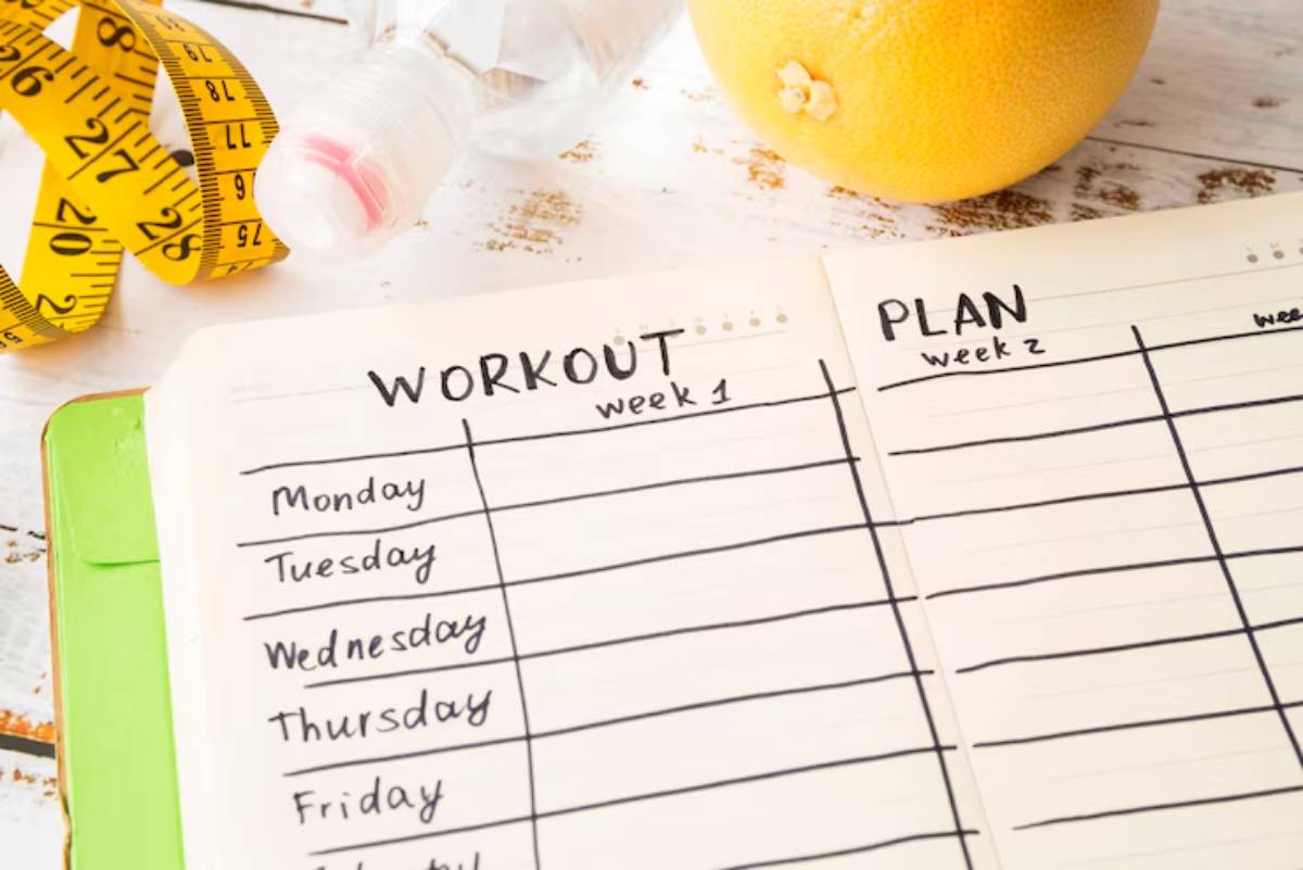 A fitness planner open to a Workout and Plan section, surrounded by a measuring tape, water bottle, and grapefruit.
