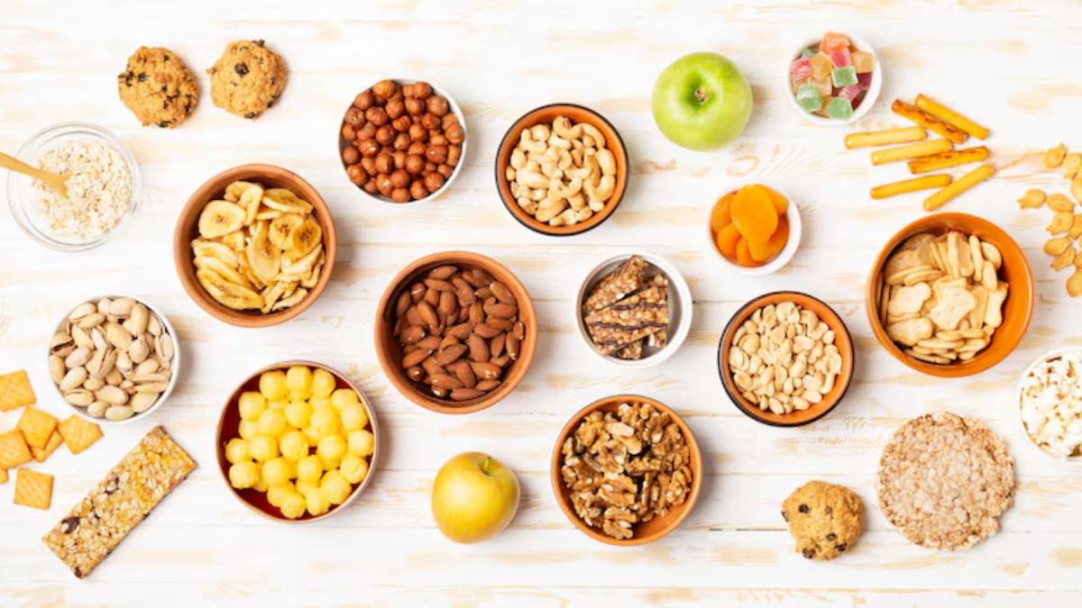 A variety of healthy snacks laid out on a table, including nuts, dried fruits, cookies, and granola bars in bowls and dishes.