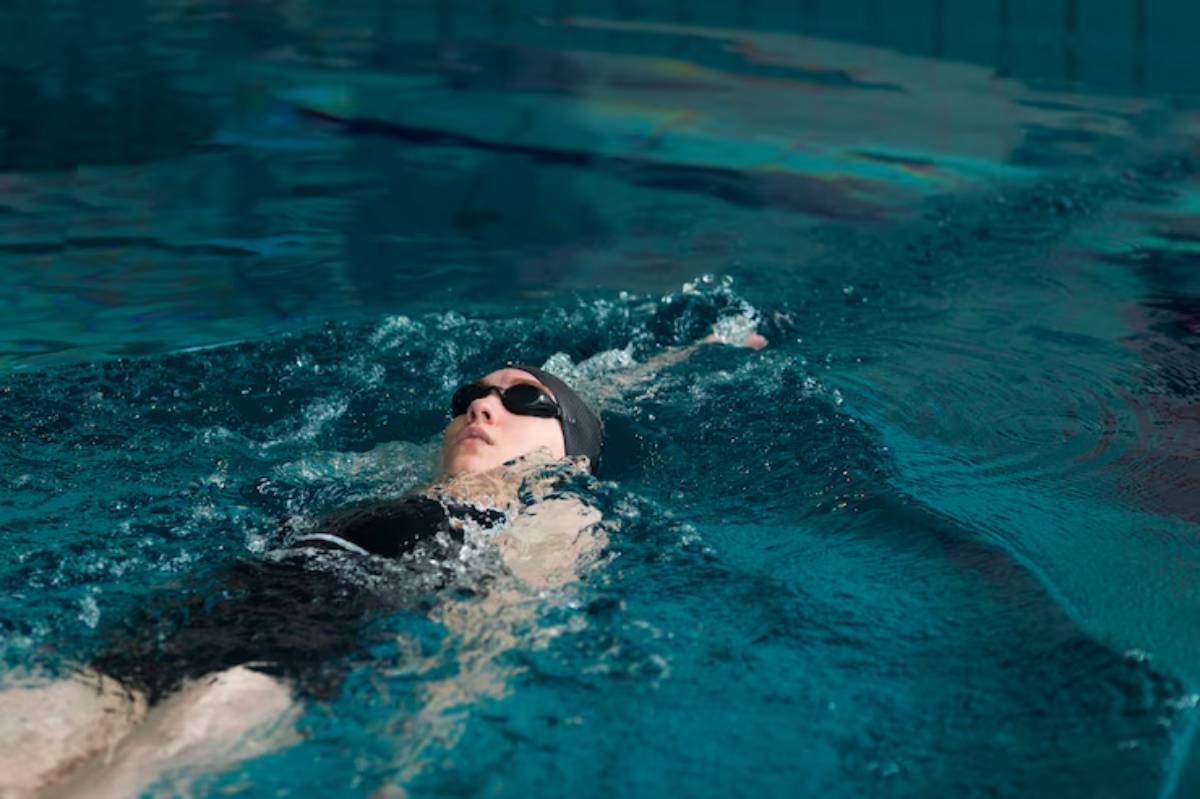 A swimmer glides through a sparkling blue pool, creating ripples in the water with graceful strokes.