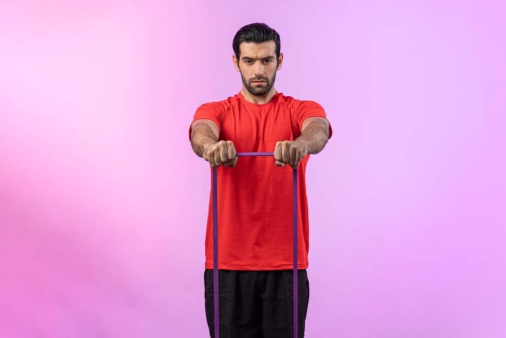 A person in a red shirt exercises with a resistance band, set against a vibrant pink background.
