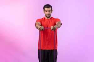A person in a red shirt exercises with a resistance band, set against a vibrant pink background.