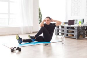 A person in athletic wear performs abdominal exercises on a blue mat in a bright room with a dumbbell and water bottle nearby.