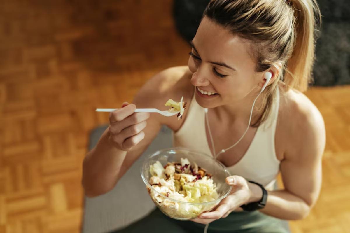 A person holding a bowl of salad with vegetables, listening to music through earphones in a cozy, wood-paneled setting.