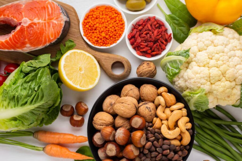 A colorful assortment of fresh vegetables, salmon, nuts, and seeds arranged on a white surface, showcasing healthy foods.