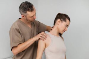 A healthcare professional examines a patient's shoulder in a clinical setting, focused on physical therapy techniques.
